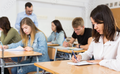 Young girl is writing test and thinking about questions at the desk