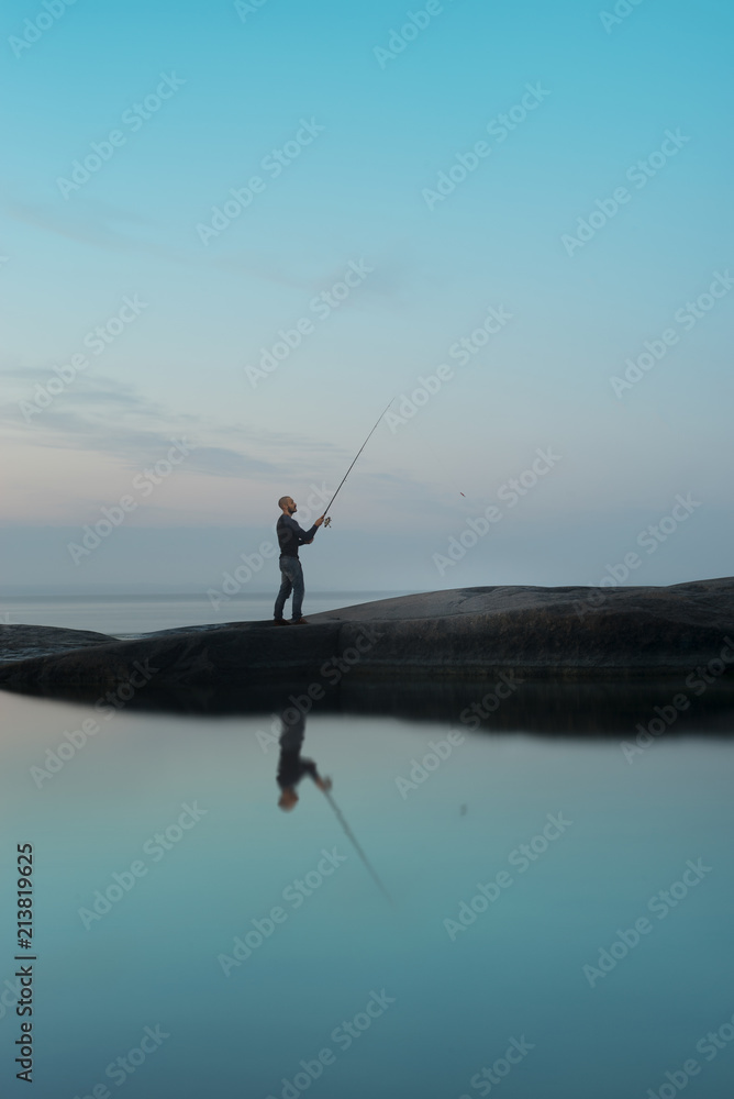 A fisherman is fishing on a stone island during the white nights A fisherman is fishing on a stone island during the white nights