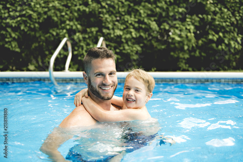 Cute little boy learning to swim with parents in pool