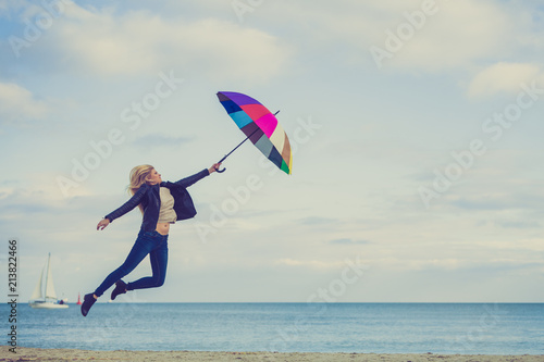 Woman jumping with colorful umbrella on beach © anetlanda