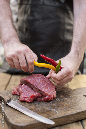 Men's hands and steaks of meat. Preparation of dinner man. Wooden table and old board. Beef and bitter colored pepper. Copy space.