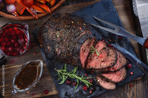 Appetizing roast beef with sauce and spices on a wooden table next to grilled vegetables