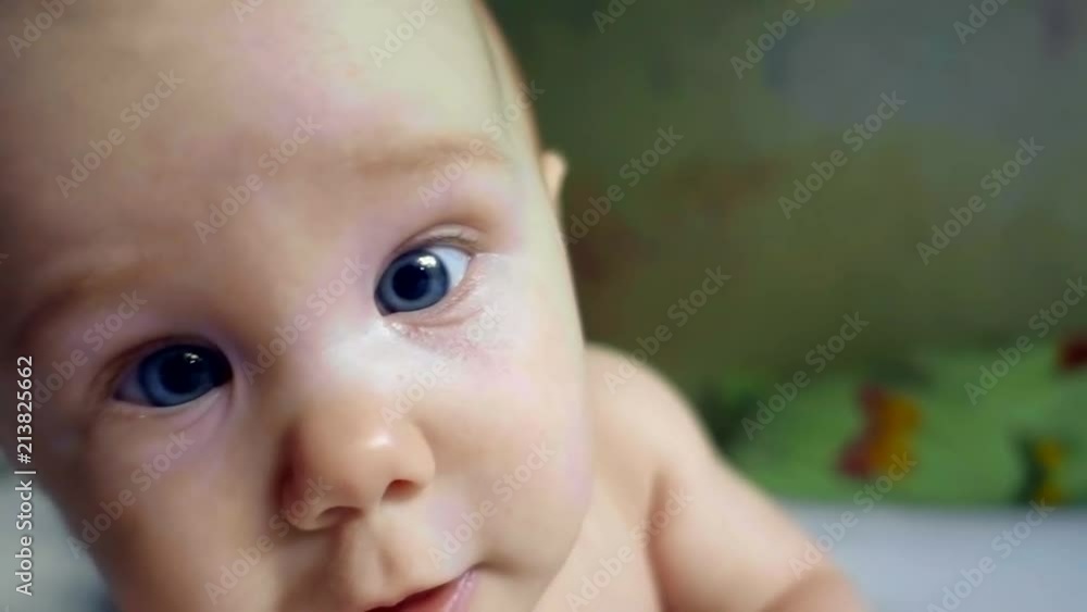 little child is lying on a belly in a bed and stretching hands to camera, looking forward little child is lying on a belly in a bed and stretching hands to camera, looking forward
