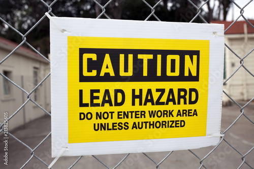 Photos CAUTION LEAD HAZARD sign attached to chain link fence.