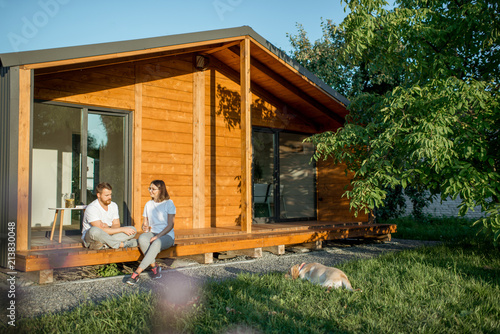 Young lovely couple sitting with dog on the terrace on the backyard of their wooden country house