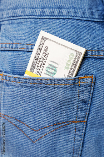 Closeup bundle of 100 dollar bills sticking out of a blue jeans pocket