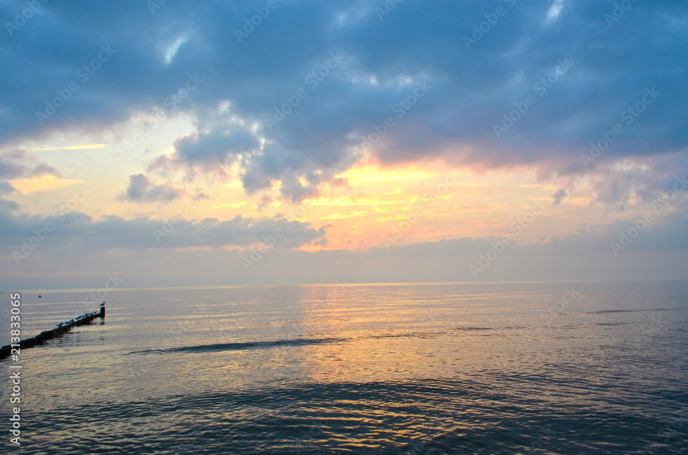 Fototapeta premium Blue and orange light while a sunrise over the Baltic Sea on Usedom, Germany, with wave-breakers and seagulls sitting on them against the light