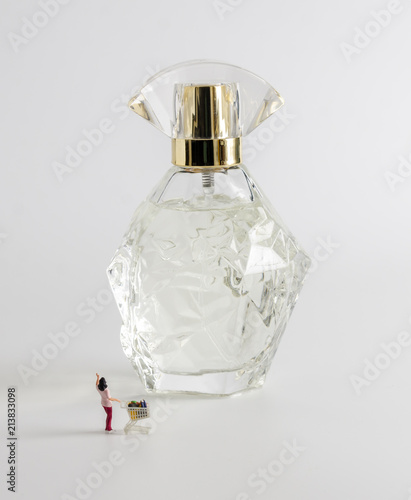 miniature figure women with shopping cart standing in front of perfume bottle
