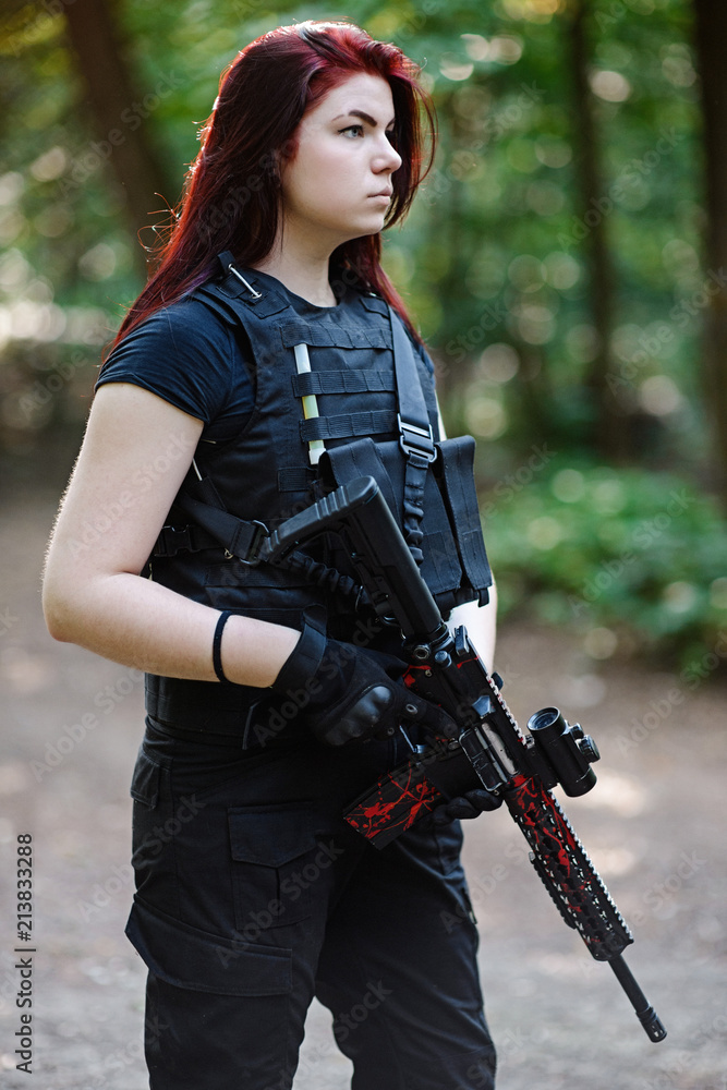 Fototapeta premium Young woman with red hair and rifle in hands