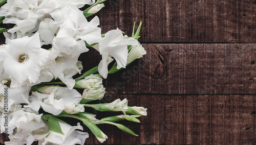 beautiful white gladioluses on rustic wooden background top view. stylish gladioli on rustic brown wood, space for text, holiday greeting card. floral flat lay, spring image photo