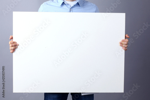 Businessman holding a blank board, standing on grey background