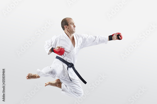 An athlete in karategi trains a swings to hit with a hand in a jump