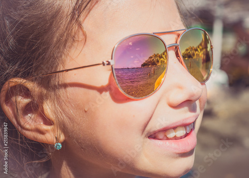 Beautiful young girl in sunglasses with beach reflection. Holidays, travel, vacation and happiness concept.
