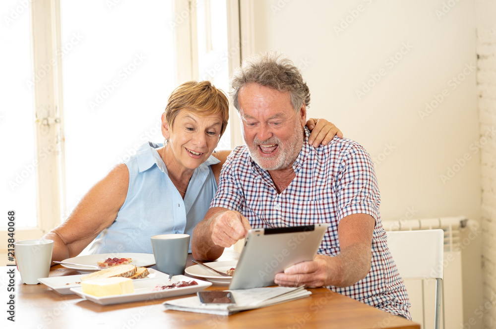 Beautiful senior retired old couple using digital tablet with joy while having breakfast at home Beautiful senior retired old couple using digital tablet with joy while having breakfast at home