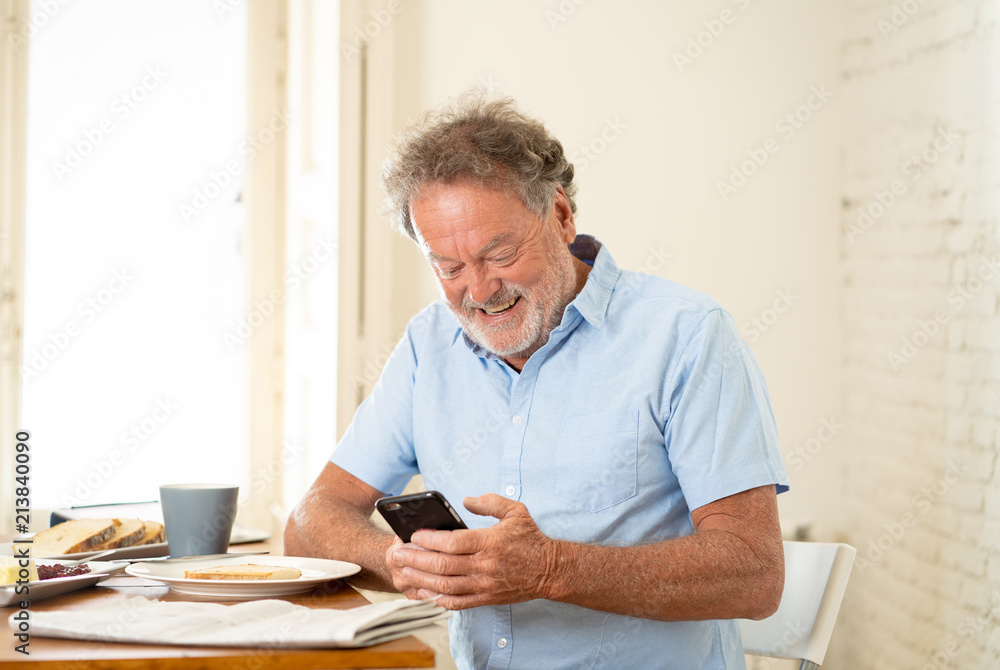 Handsome senior retired old man using mobile phone with joy while having breakfast at home Handsome senior retired old man using mobile phone with joy while having breakfast at home