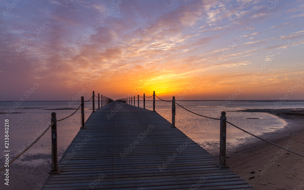 Pier reaching into the Egyptian sea at sunset with a backdrop of clouds and golden setting sun