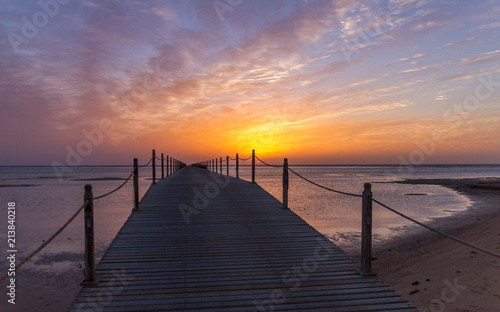 Fototapeta Naklejka Na Ścianę i Meble -  Pier reaching into the Egyptian sea at sunset with a backdrop of clouds and golden setting sun