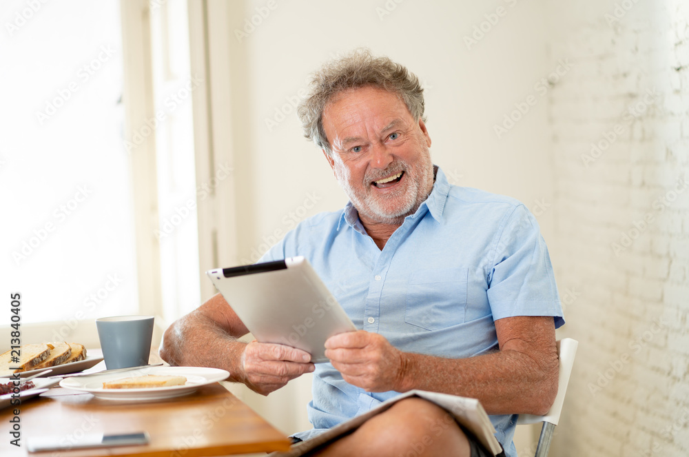 Handsome senior retired old man using tablet with joy while having breakfast at home Handsome senior retired old man using tablet with joy while having breakfast at home