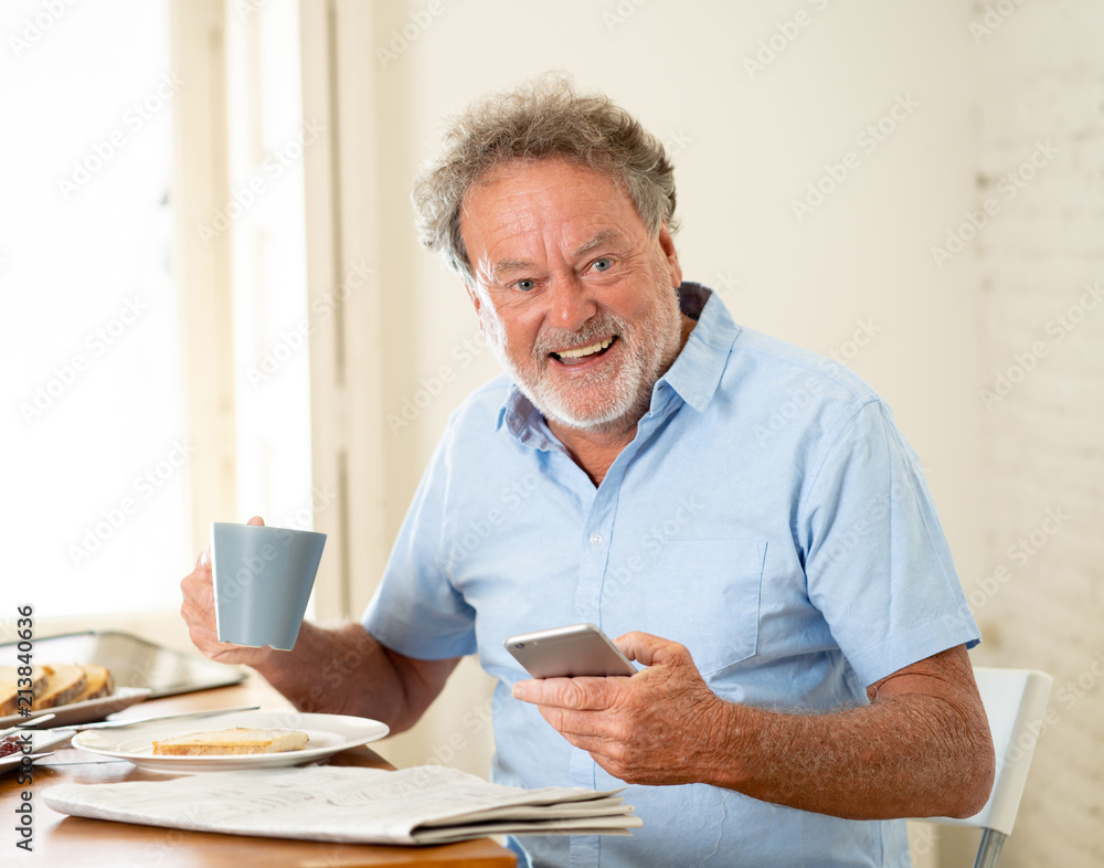 Handsome senior retired old man using mobile phone with joy while having breakfast at home Handsome senior retired old man using mobile phone with joy while having breakfast at home