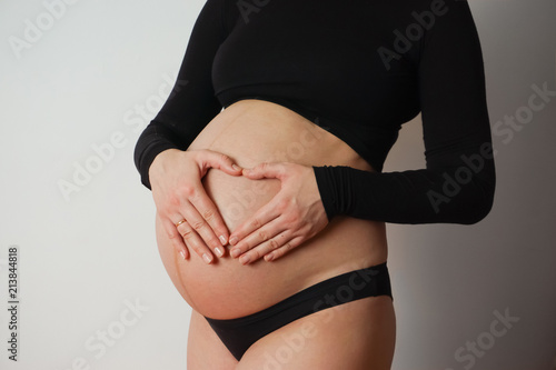 pregnant woman in black holds hands with a heart