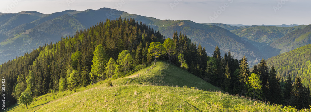 Scenic panoramic shot taken at spring evening with warm side light. Mountains covered with forest and meadows. Concept of clear environment, ecology concept. Natural background.