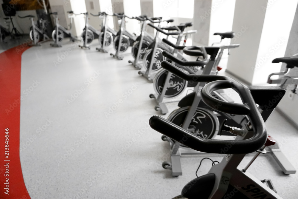 Fototapeta premium Modern gym interior with equipment. Row of training exercise bikes detail, backlight. Healthy lifestyle concept