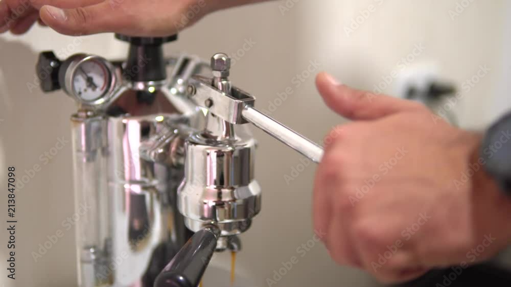 The hand presses on the metal arm of a coffee machine. Making coffee in an old coffee machine. coffee is poured under the pressure of the lever. The hand presses on the metal arm of a coffee machine. Making coffee in an old coffee machine. coffee is poured under the pressure of the lever.