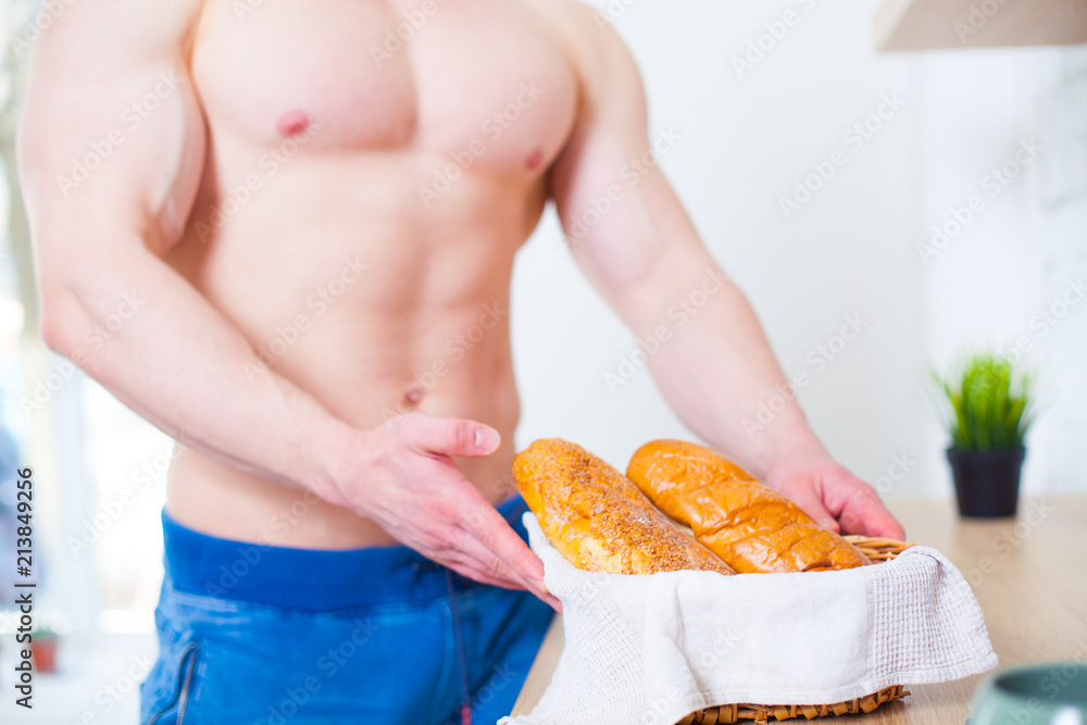 Muscular man with a naked torso in the kitchen with bread, concept of healthy eating. Athletic way of life.