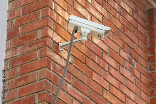 Surveillance camera attached to a brick wall overlooking a parking lot