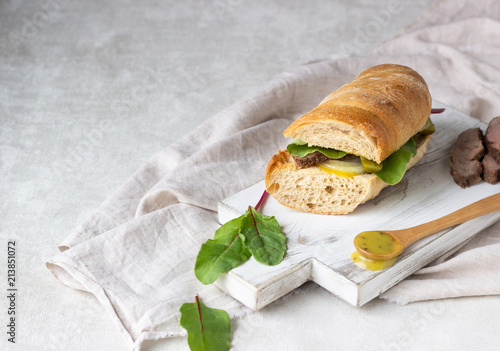 Roast beef sandwich with fresh salad, onion and cukes and mustard sauce on white wood cutting board