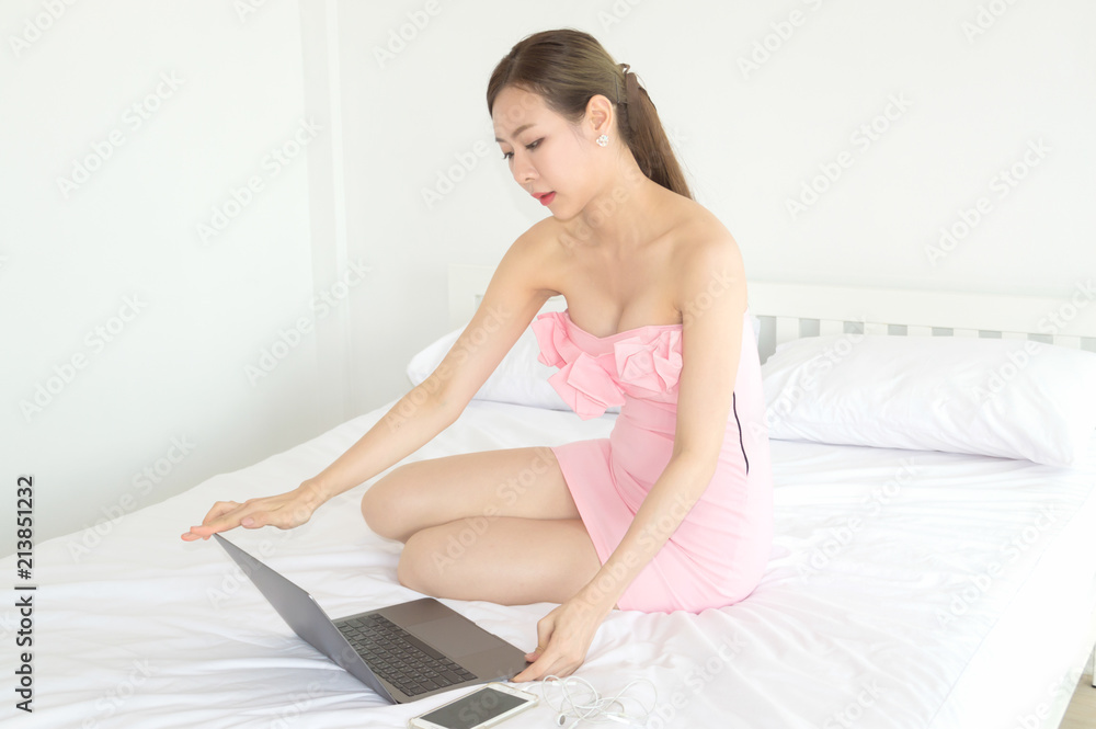Beautiful woman is working with a notebook in a white bedroom. Beautiful woman is working with a notebook in a white bedroom.