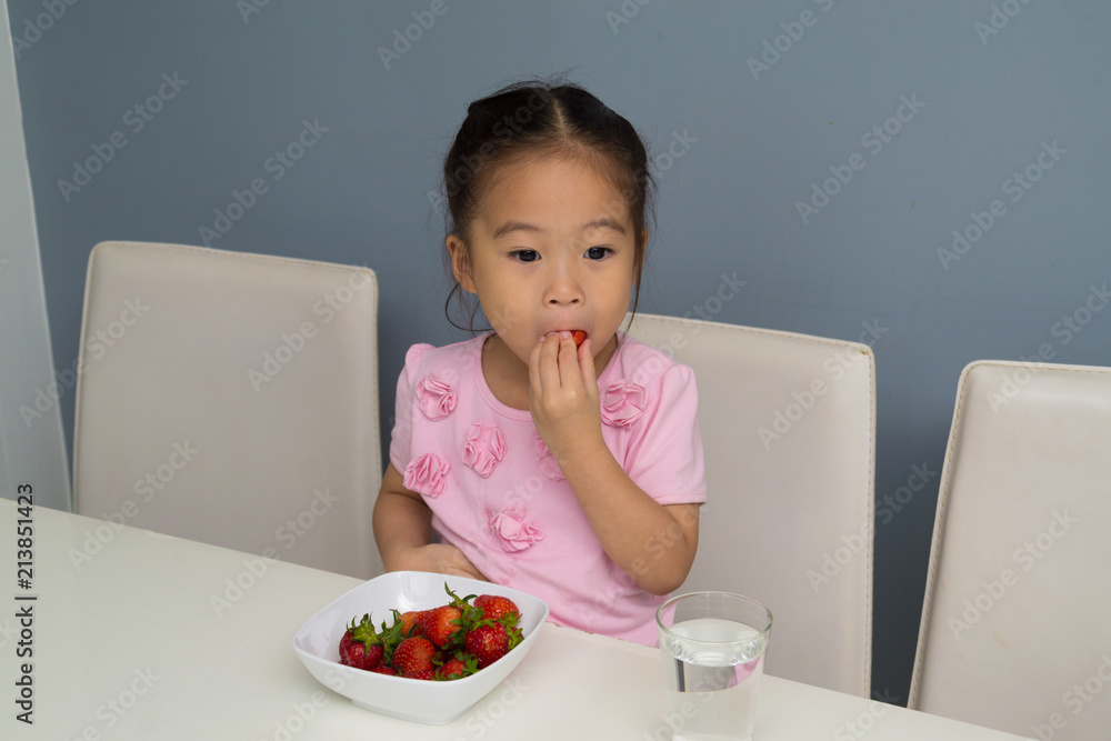 .The girl is eating strawberry in the kitchen. .The girl is eating strawberry in the kitchen.