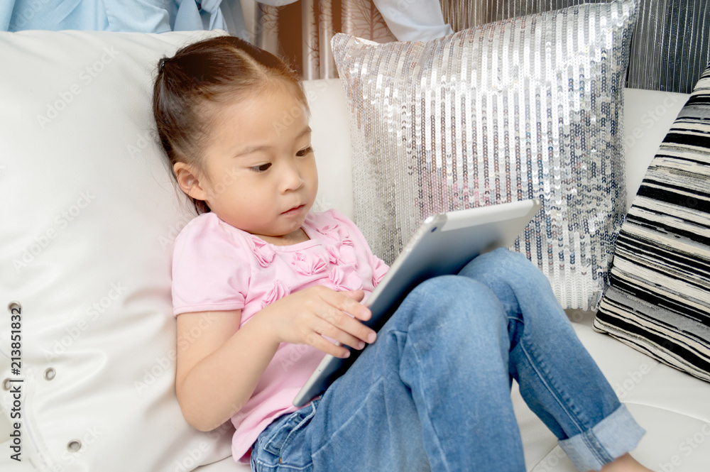 The girl is playing the .tablet playfully on the couch. The girl is playing the .tablet playfully on the couch.