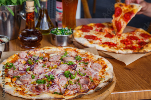 Hot delicious pizza with sausage, paprika and red onion on wooden restaurant table.