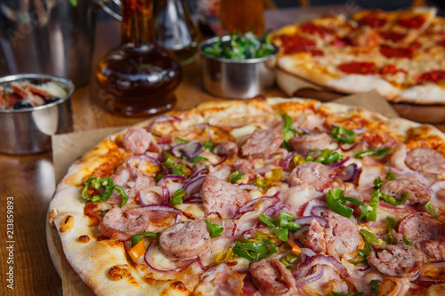 Hot delicious pizza with sausage, paprika and red onion on wooden restaurant table..