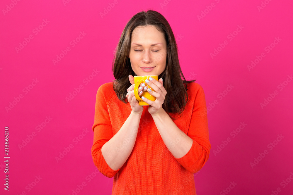 Beautiful brunette woman with a yellow cup in hands on a pink background. Drink hot drinks and be healthy. Beautiful brunette woman with a yellow cup in hands on a pink background. Drink hot drinks and be healthy.