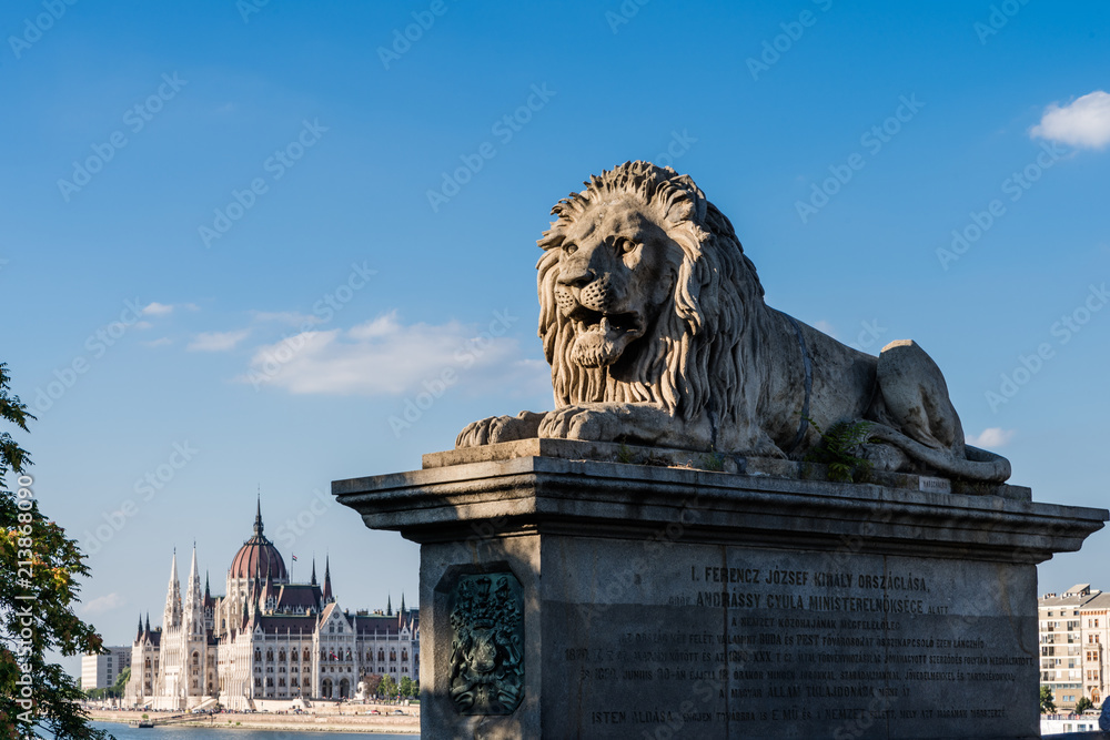Budapest – Löwenstatue am Brückenkopf der Kettenbrücke mit Parlamentsgebäude im Hintergrund