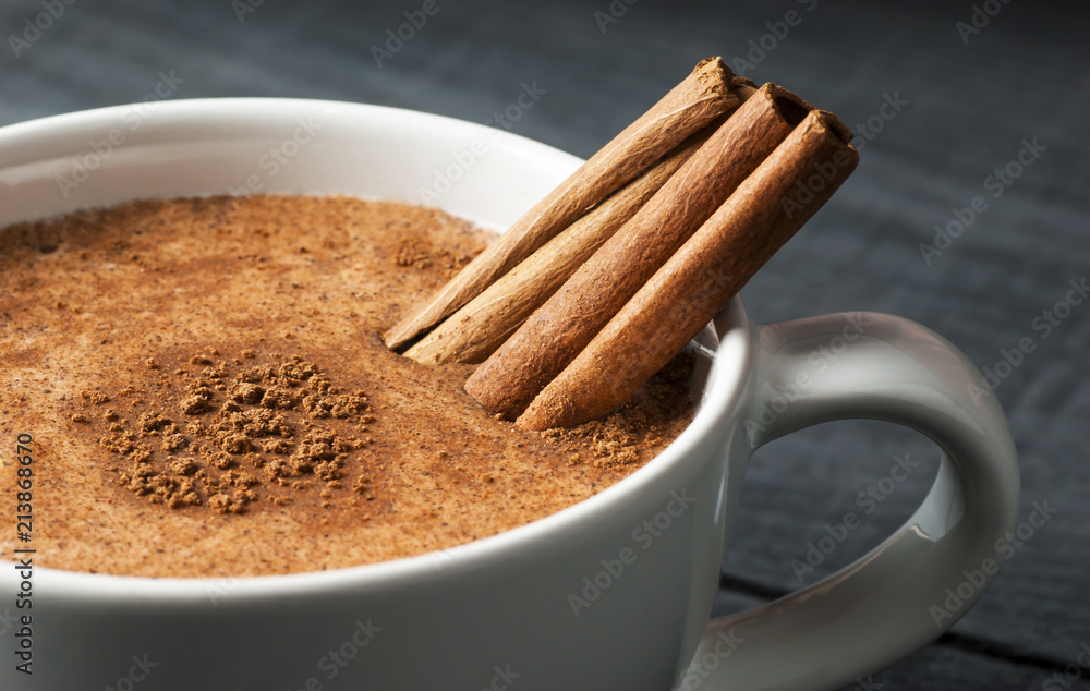 Close up white cup of salep milky hot drink of Turkey with cinnamon powder healthy spice on black wooden background - obrazy, fototapety, plakaty 