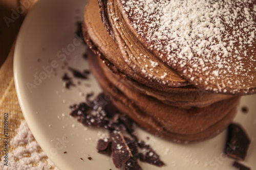 A view of delicious cocoa pancakes with dark chocolate and powdered sugar on a wooden table photo