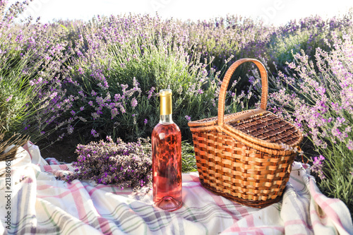 Fototapeta Naklejka Na Ścianę i Meble -  Bottle of wine and basket on blanket in lavender field