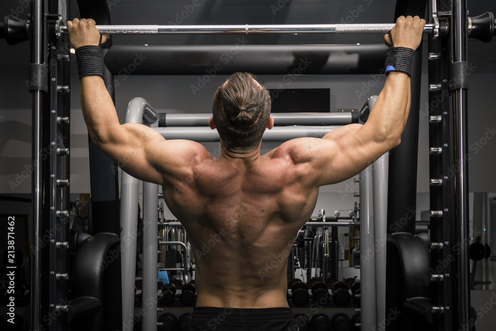 Hombre fuerte con grandes músculos haciendo dominadas en el gimnasio de espaldas. Ponerse en forma. Hombre fuerte con grandes músculos haciendo dominadas en el gimnasio de espaldas. Ponerse en forma.
