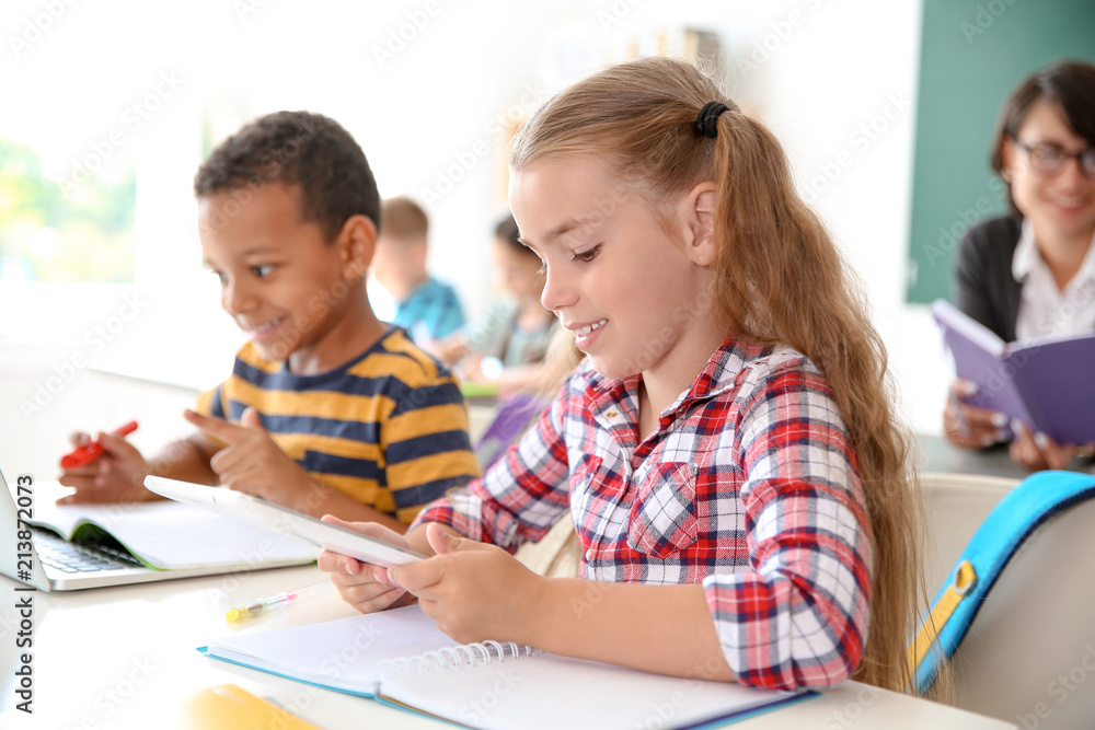 Cute little children with gadgets sitting at desk in classroom. Elementary school Cute little children with gadgets sitting at desk in classroom. Elementary school