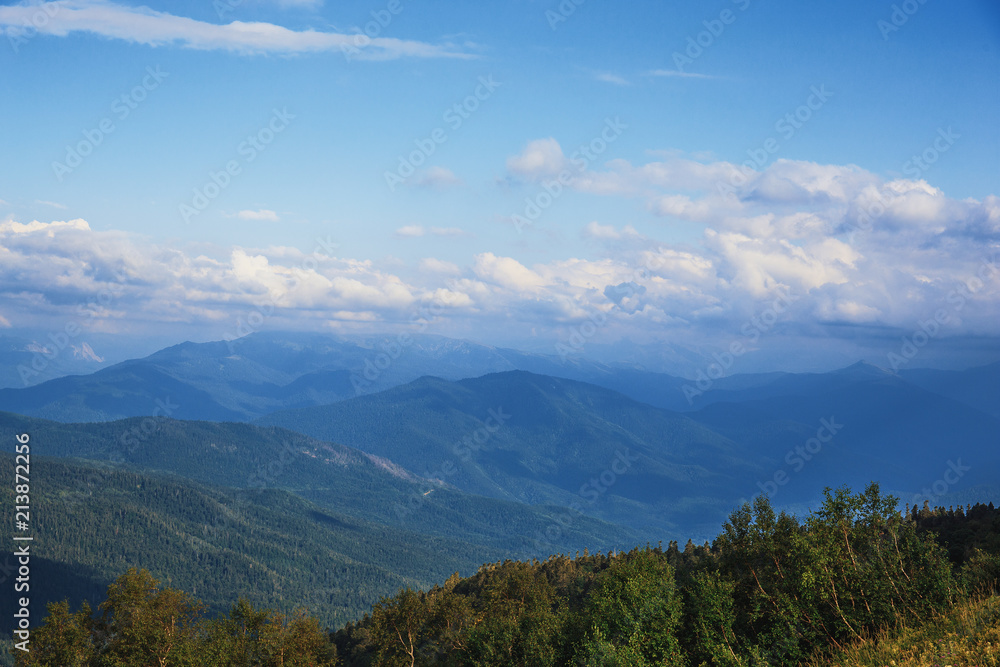 Majestic mountains landscape panorama. Bright blue sky with fluffy clouds and ranges of mountains in myst