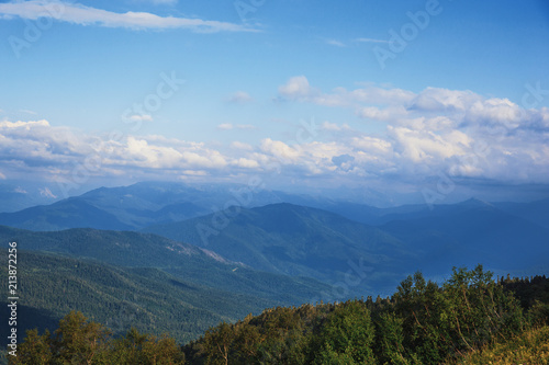 Majestic mountains landscape panorama. Bright blue sky with fluffy clouds and ranges of mountains in myst