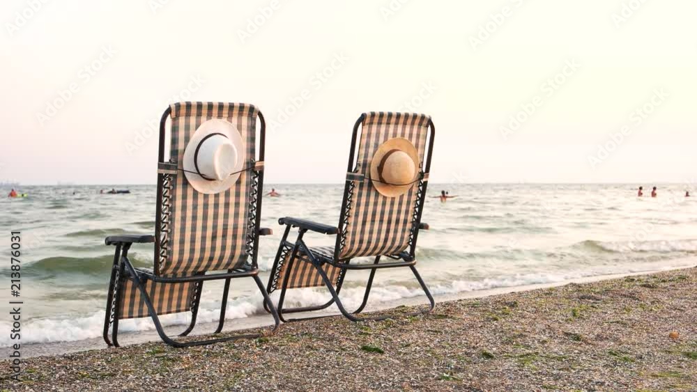 Deck chairs on beach seashore. Attached hats. Rear back view. Deck chairs on beach seashore. Attached hats. Rear back view.