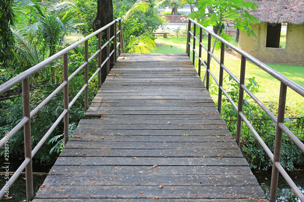 Old wooden bridge with metal rail in public park.
