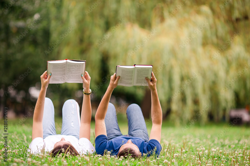 Relaxed young couple reading books while lying on grass