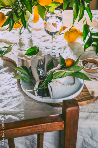 Table setting with white plate, cutlery, linen napkin and orange tree branch decoration on white linen tablecloth . Close up. Table with table setting and shair photo