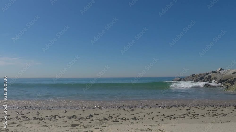 Seascape of waves crashing onto a California beach covered in shells by a rocky pier, summer day Seascape of waves crashing onto a California beach covered in shells by a rocky pier, summer day