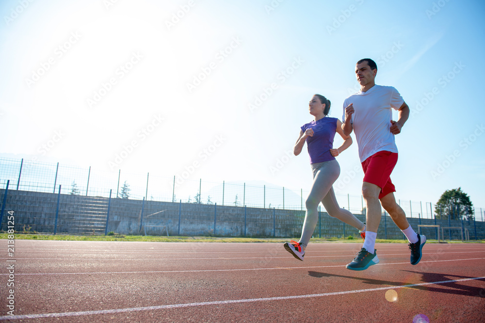 Young sportive couple warming up legs before jogging on running track at sports stadium